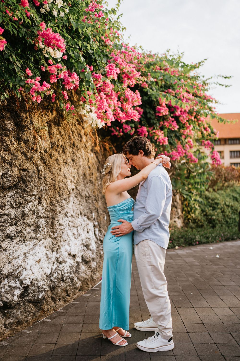 A romantic moment shared against a wall covered in vibrant pink bougainvillea flowers.