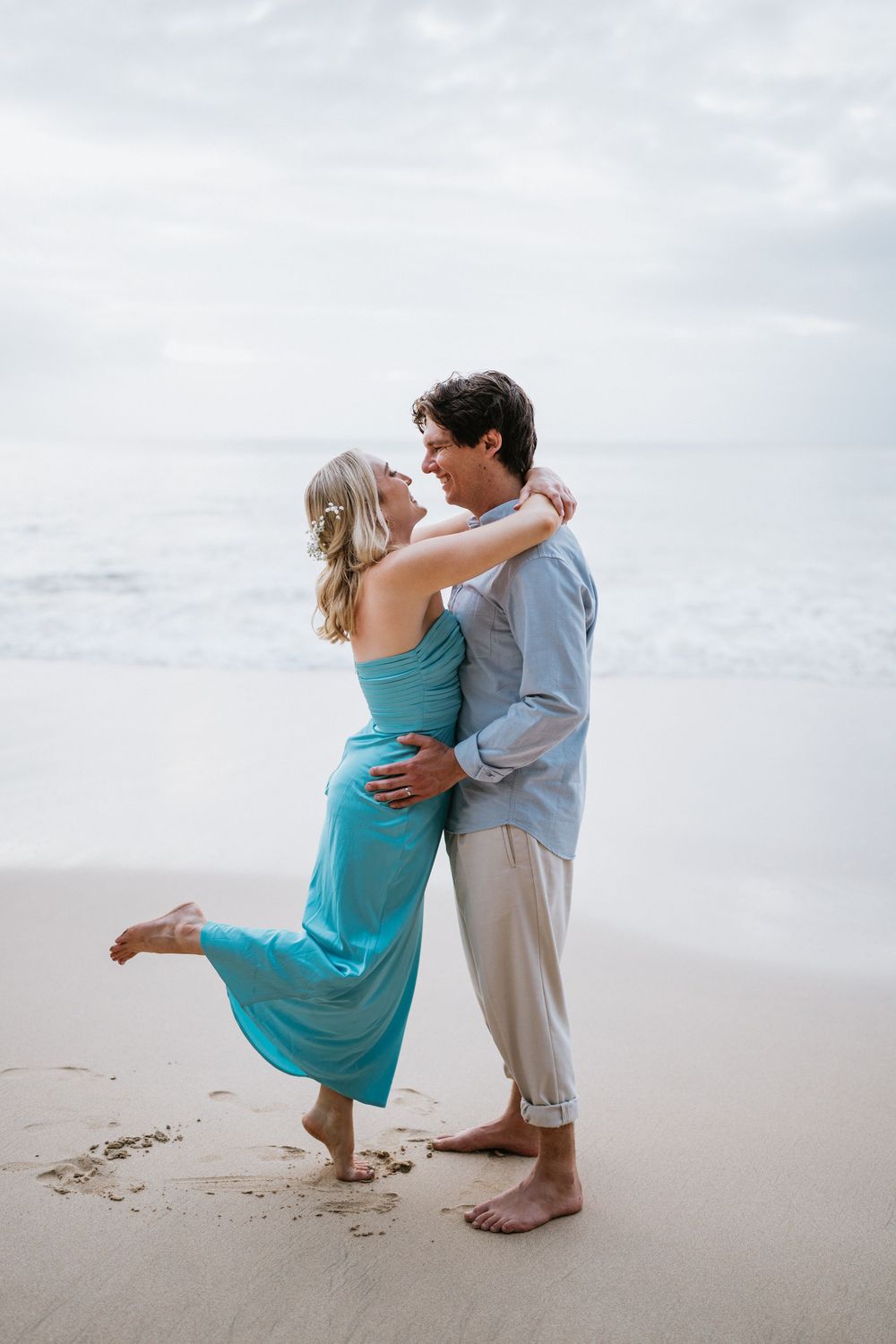 A couple shares an intimate dance moment on a sandy beach with cloudy skies.