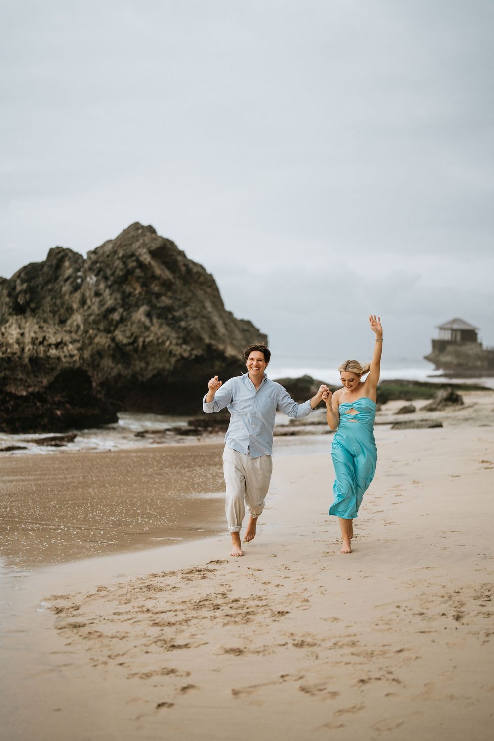 A couple runs and plays together along a scenic beach with dramatic rock formations.