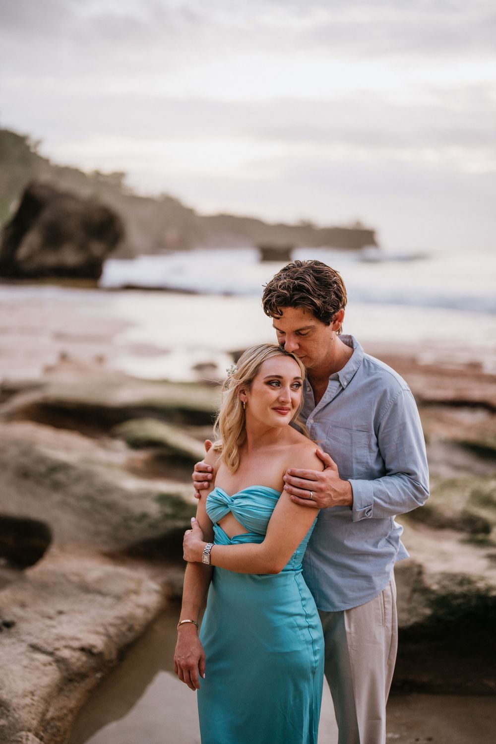 A tender moment between a couple on rocky beach cliffs during an overcast day.