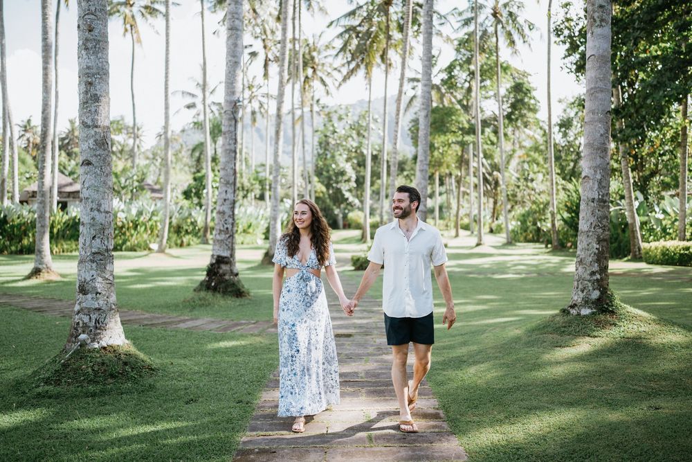 Couple walking hand in hand down a palm-lined path in a tropical garden.
