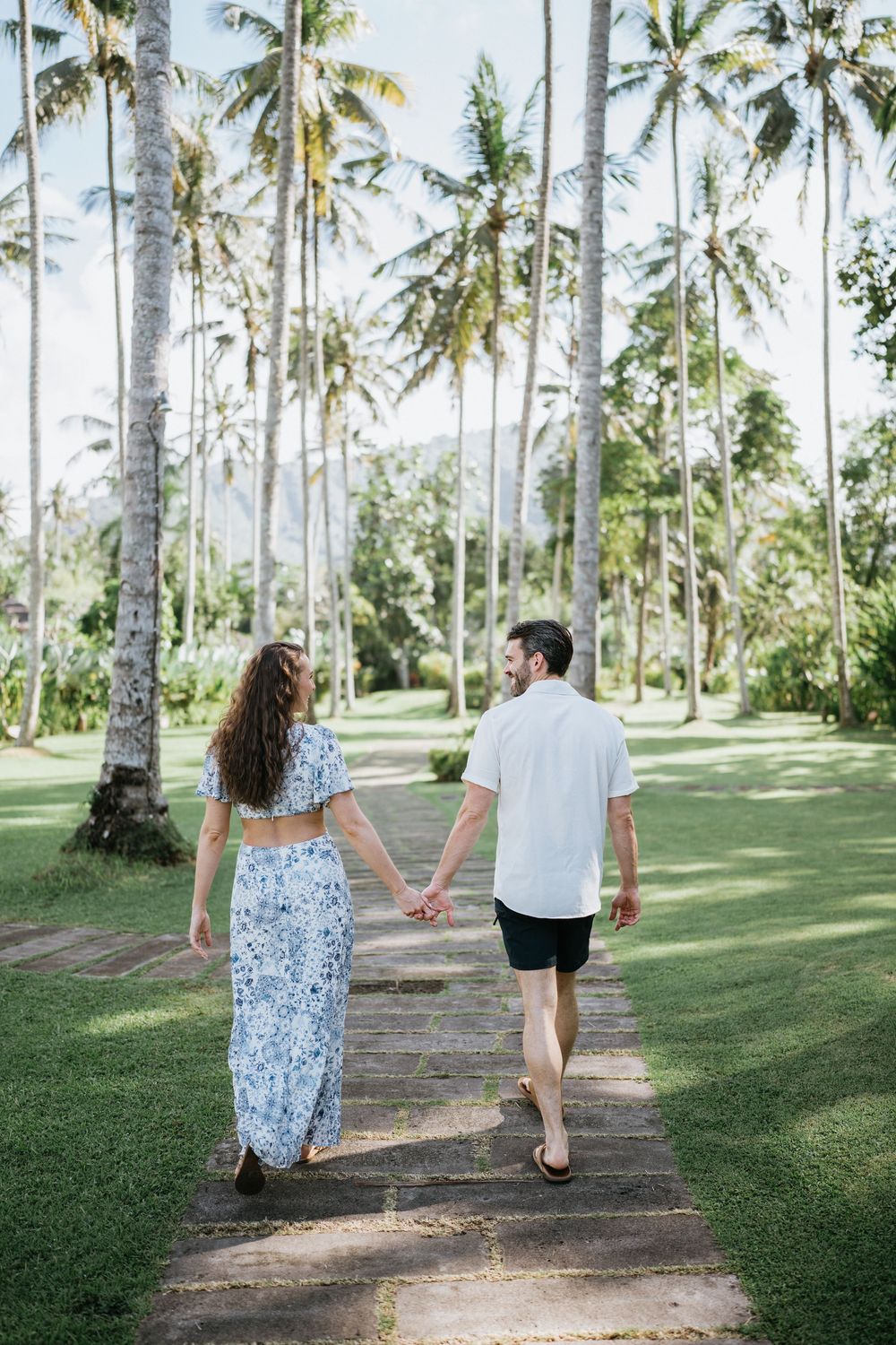 Couple walking together on a dirt path surrounded by towering palm trees.