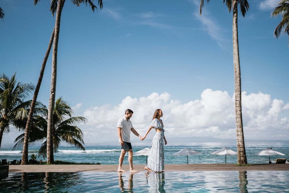 Couple enjoying a romantic moment by an infinity pool overlooking the ocean with palm trees and blue skies.