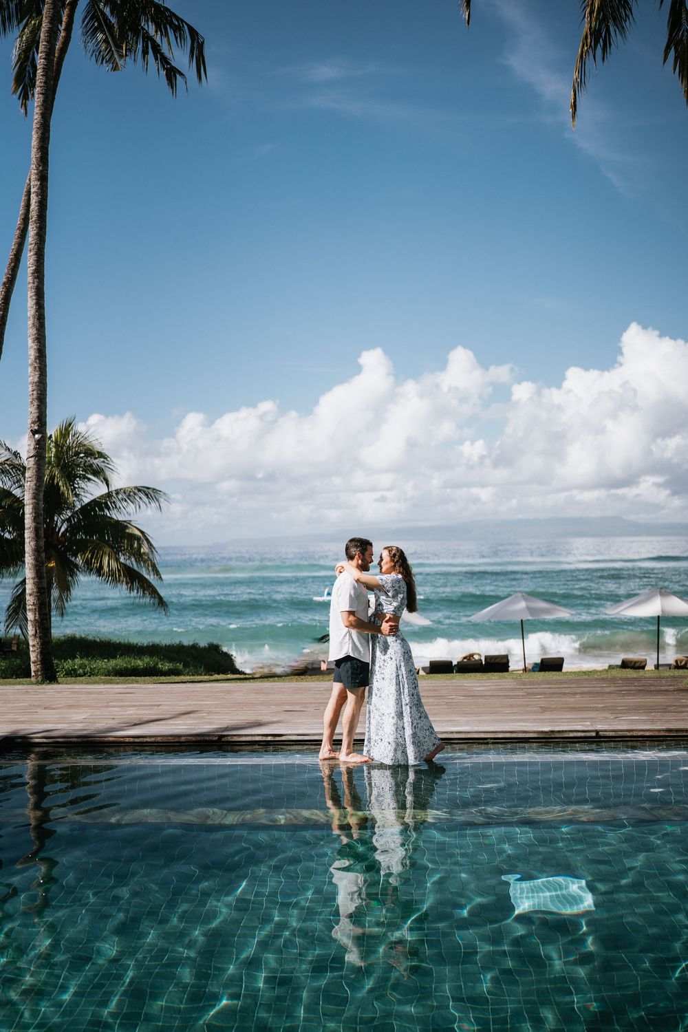 Couple sharing intimate moments beside a beachfront infinity pool surrounded by palm trees.