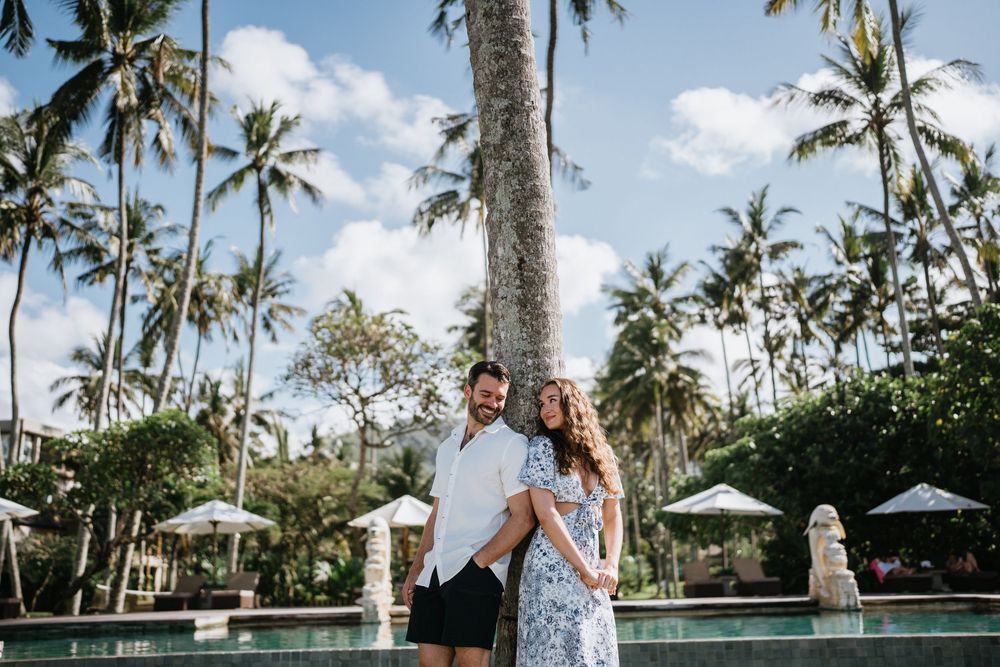 Romantic photo session on wooden deck with lush palm trees and resort umbrellas.