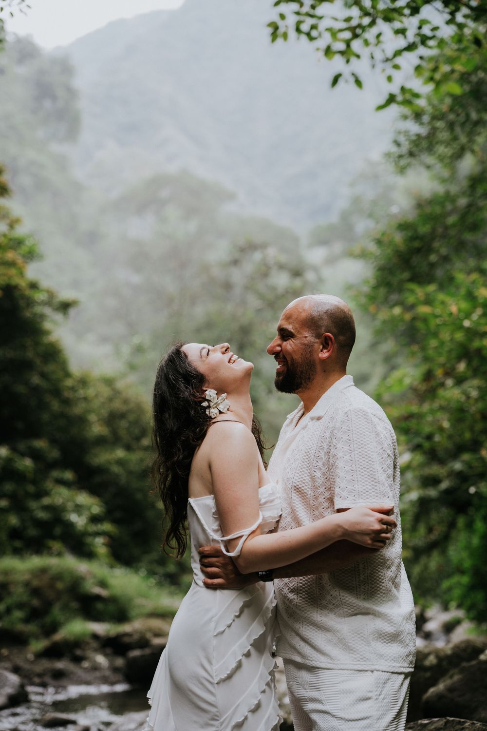 A couple embraces and laughs together in a misty mountain landscape.
