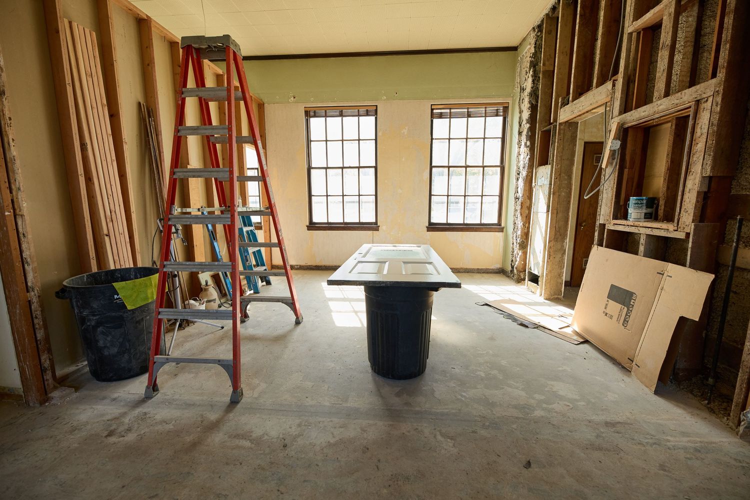 Construction site showing exposed walls, ladders, and windows in a renovation project.
