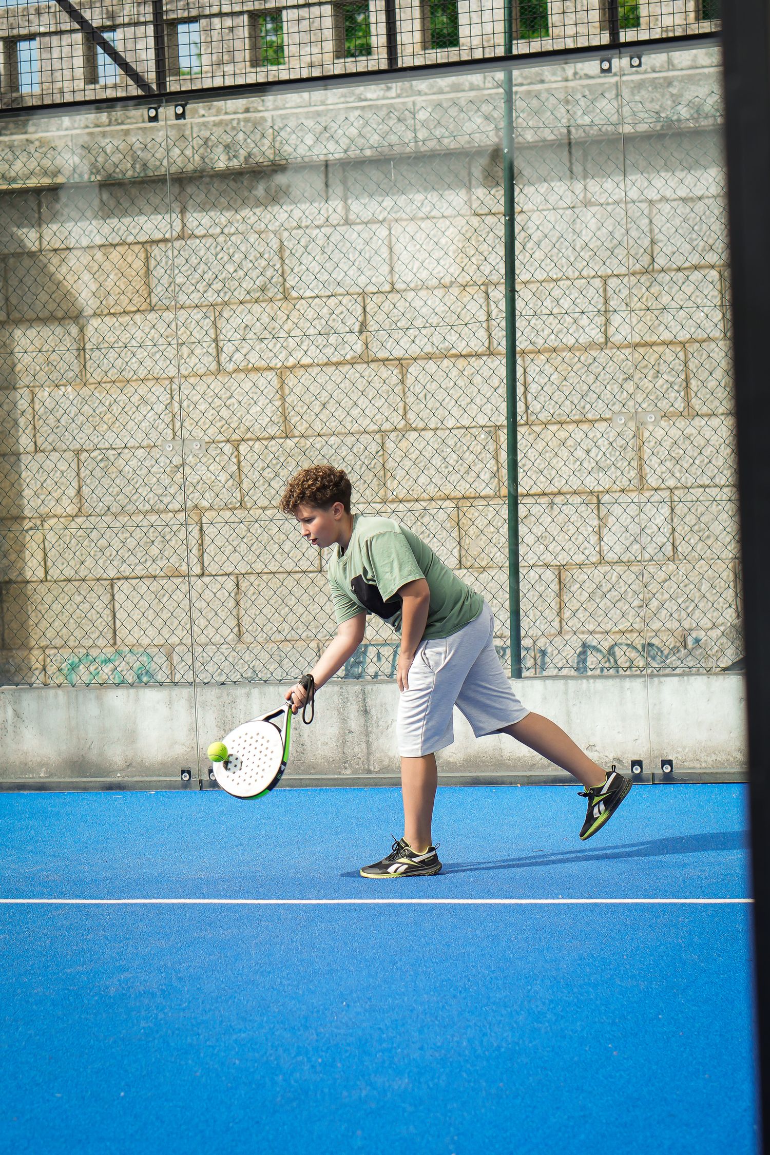 Tennis player practicing serves on a blue court against a concrete wall.