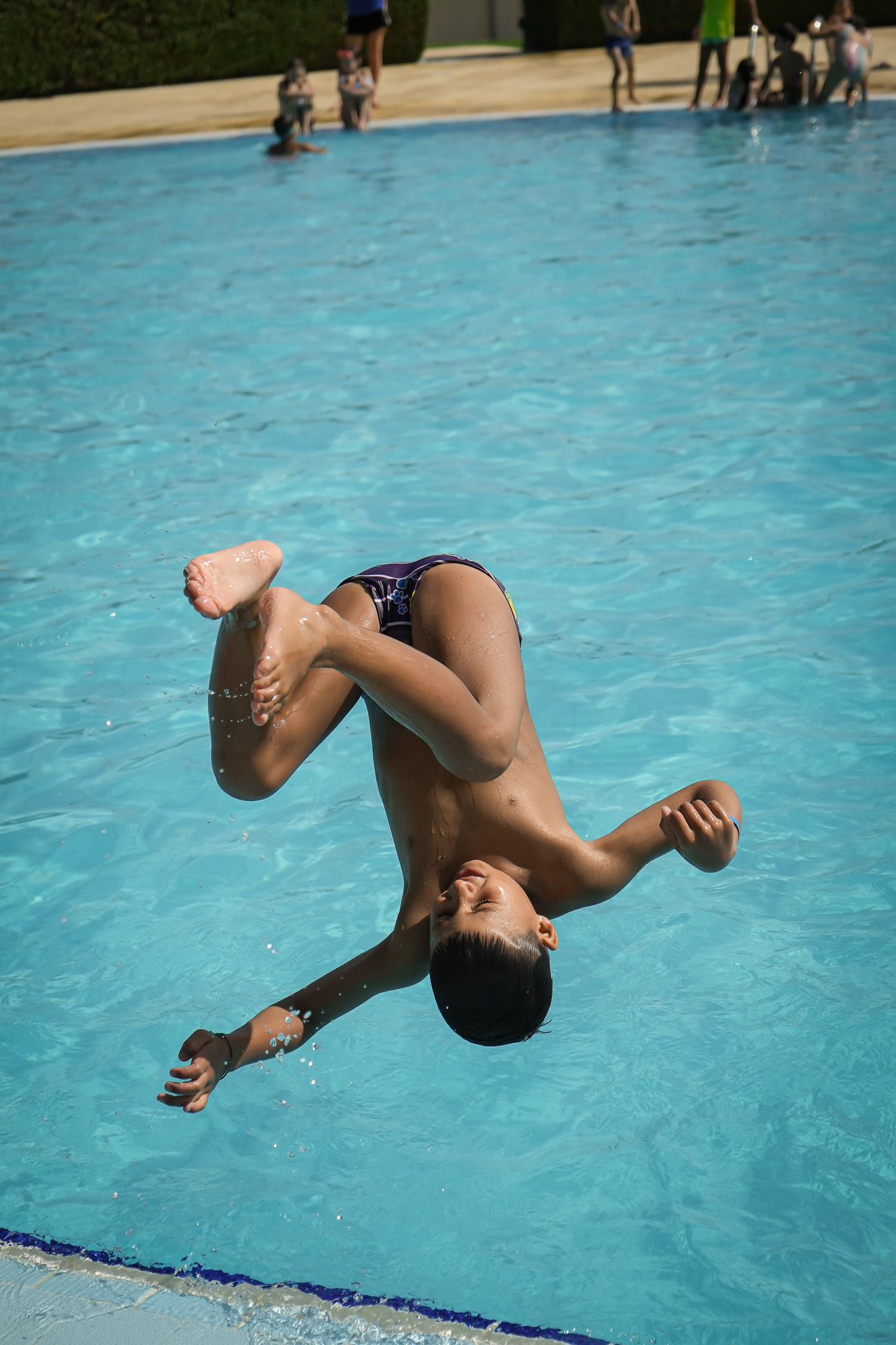 A sequence showing a backflip dive into a bright blue swimming pool.