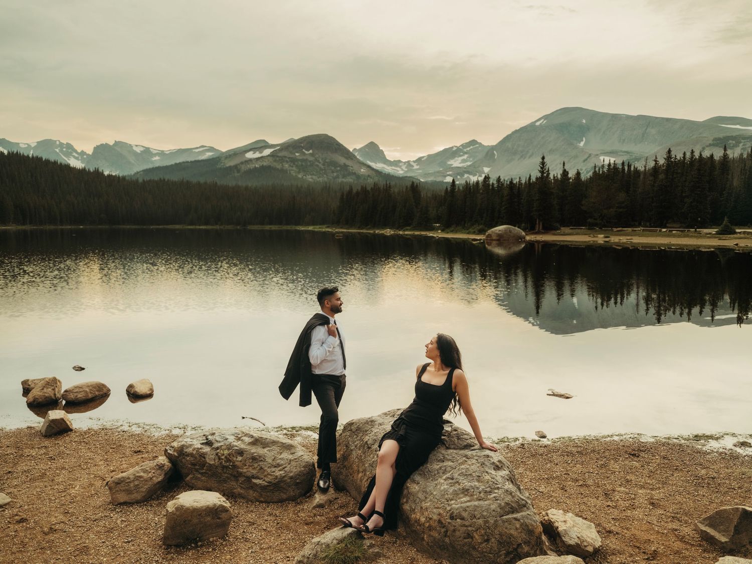 A tranquil mountain lake landscape with snow-capped peaks reflecting in calm waters at sunset.