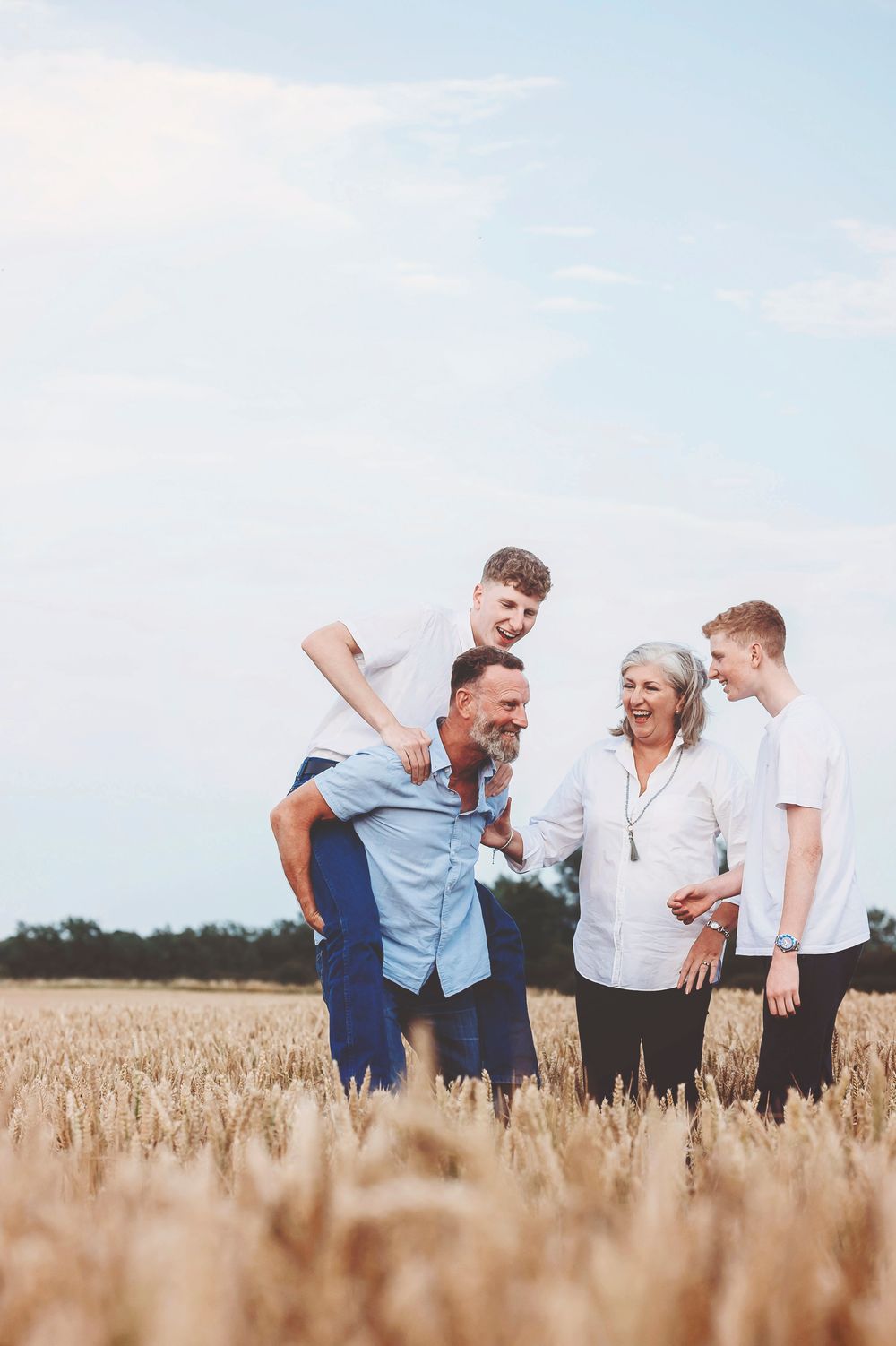 A family group laughs together while standing in a golden wheat field on a bright sunny day.