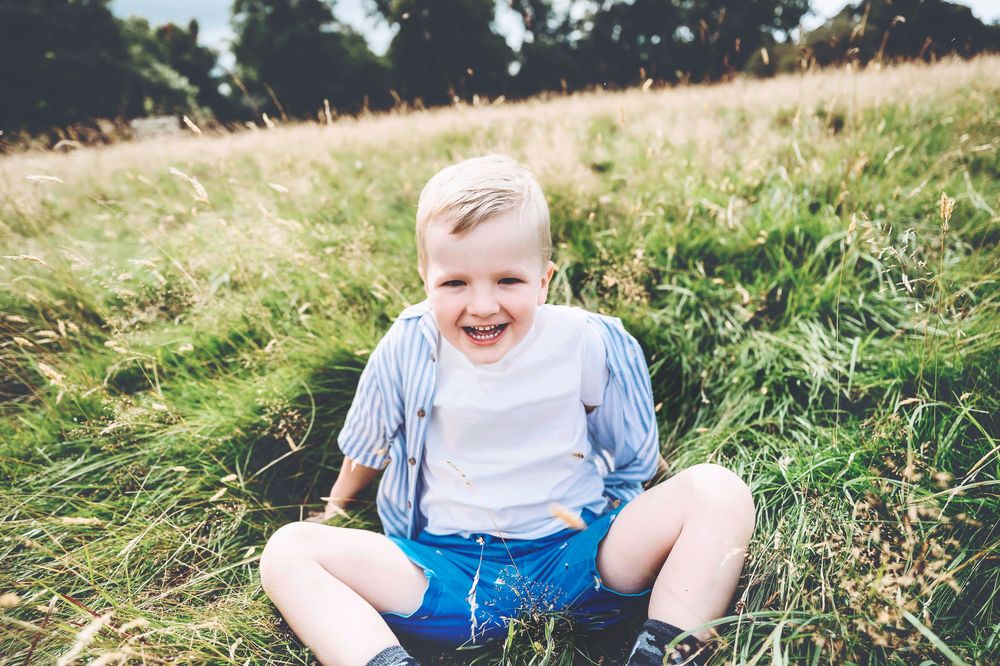 Seven sequential photos show a young person rolling down a grassy hill in a playful manner at a park.