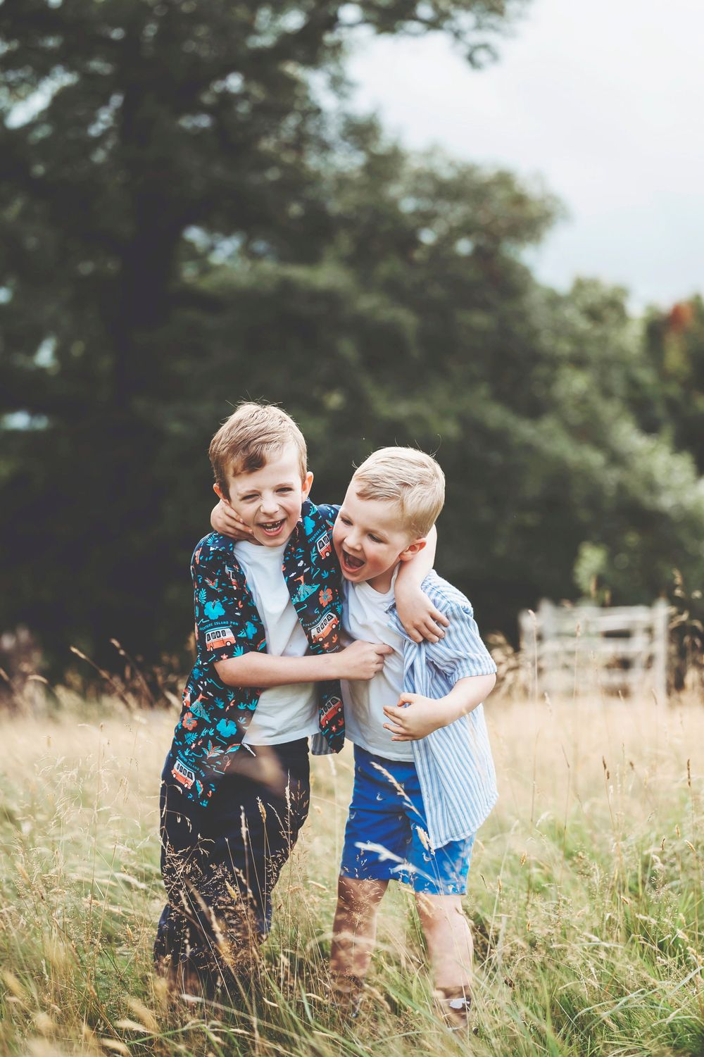 Two young children playfully hug and laugh together while standing in a golden summer field.