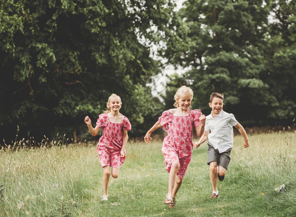 Three children run and play together through a grassy meadow on a summer afternoon.