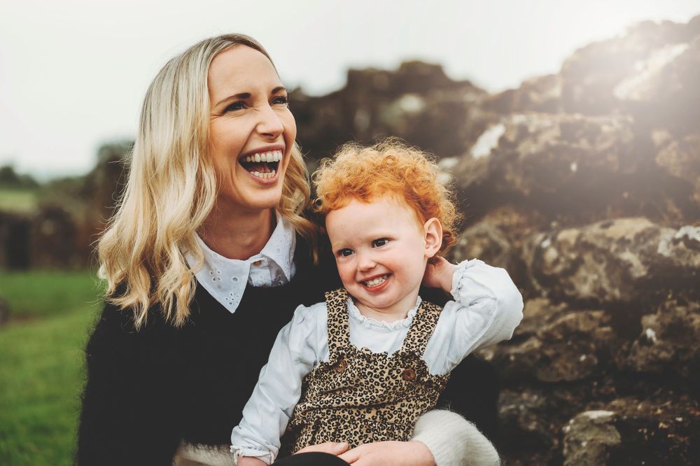 A lighthearted outdoor photography session in a sunny field shows lively interaction between parent and child.