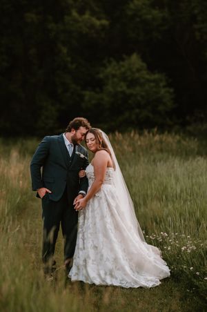 A couple in wedding attire shares an intimate moment while standing in a rustic meadow filled with wildflowers.