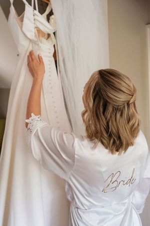 Person in white silk robe with 'Bride' embroidery getting ready for wedding ceremony from behind.