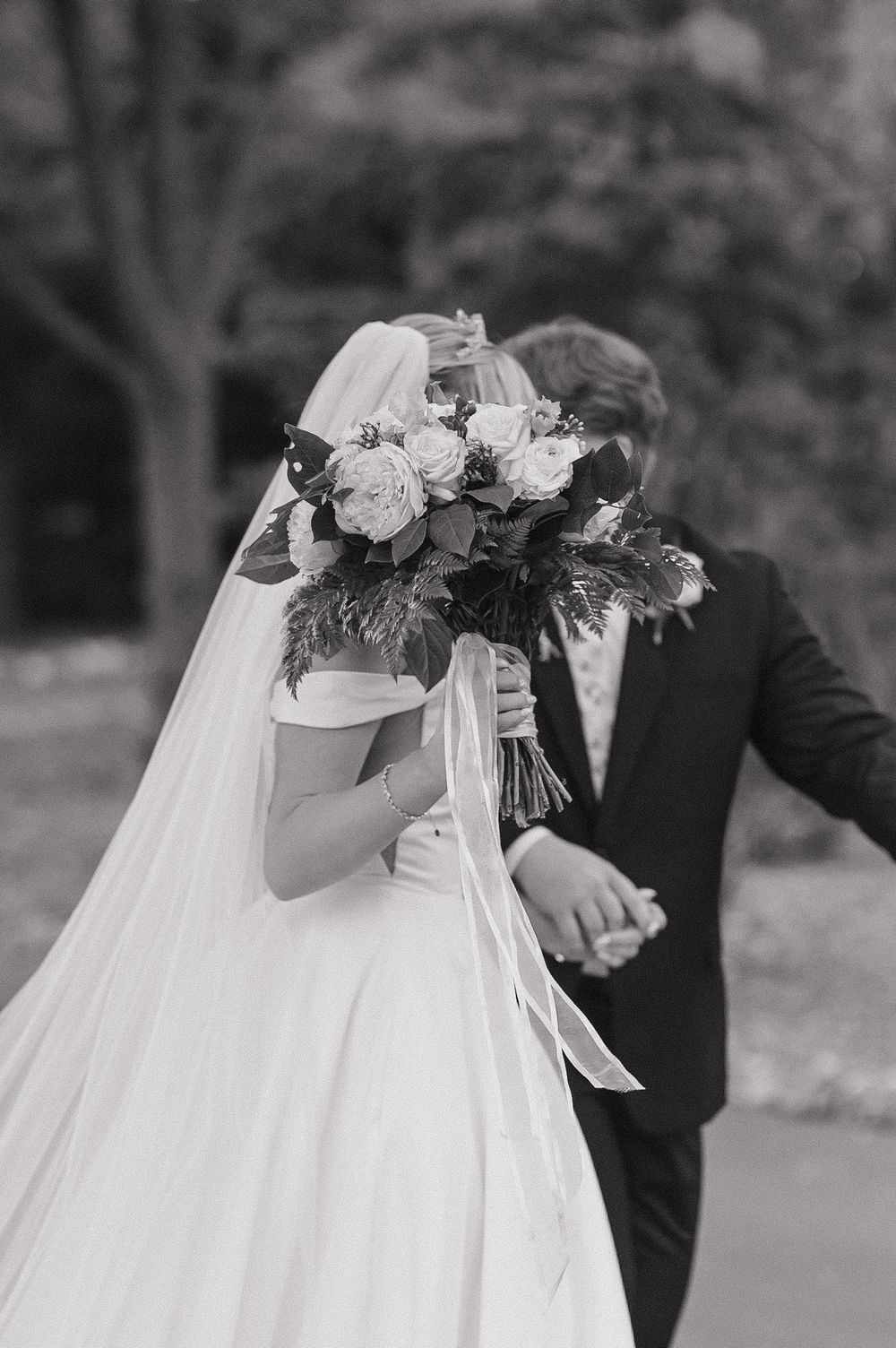Wedding couple's embracing silhouettes in black and white with flowing bridal veil and floral headpiece detail.
