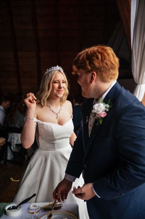 A bride and groom share a playful moment over their wedding meal while seated at a reception table.