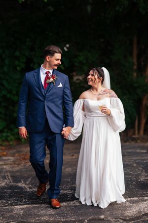 Newlyweds walking and posing together outdoors with bride in flowing white dress and groom in navy suit.