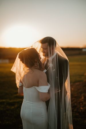 Newlyweds share an intimate moment at sunset as a delicate veil floats in the golden light.