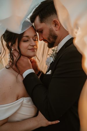 Intimate wedding portrait of newlyweds embracing in warm light with bride in off-shoulder dress and groom in black suit.