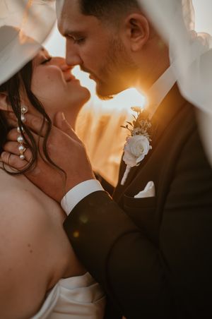 A romantic close-up portrait showing a wedding couple sharing a tender kiss in warm sunset lighting.