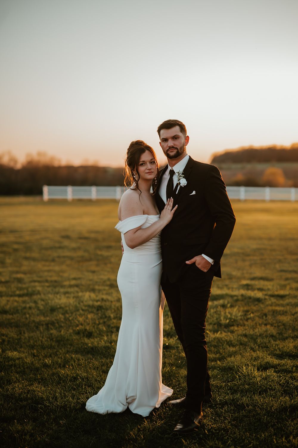 Wedding couple shares an intimate moment together during sunset in an open grassy field.