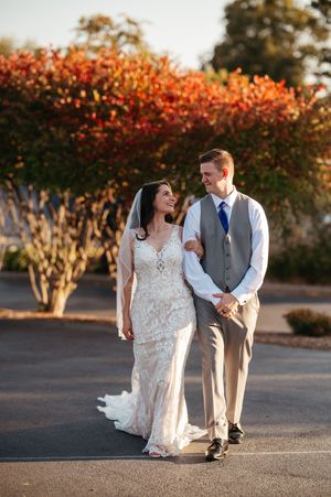 A couple in wedding attire shares a romantic moment among autumn trees during golden hour sunset.