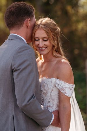 A tender moment between newlyweds in an outdoor setting with golden sunlight filtering through autumn trees.
