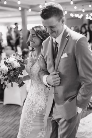 Wedding party poses in formal attire with bride in lace dress and groomsmen in gray suits.