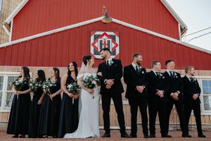 Wedding party in black attire lined up against a red barn backdrop.