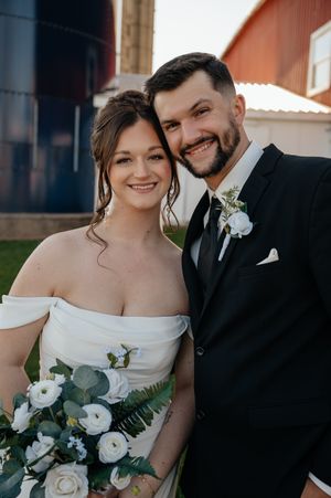 A happy couple poses together for their wedding day photos wearing traditional black tuxedo and white gown.