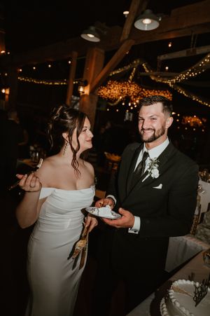 A couple dances together at their wedding reception under twinkling lights in a rustic wooden venue.