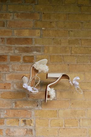 White ice skates with decorative bows and pom-poms hang on a rustic brick wall.