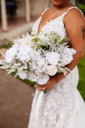 A stunning all-white bridal bouquet with roses, carnations and baby's breath against a lace wedding dress.