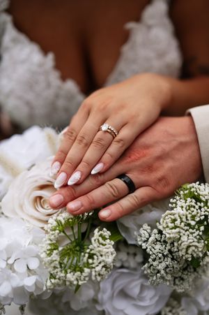 Newlywed hands with wedding rings rest on white roses and baby's breath flowers in elegant wedding bouquet.