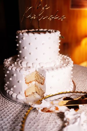 A white two-tier wedding cake with pearl-like dots and a slice cut out revealing vanilla layers inside.