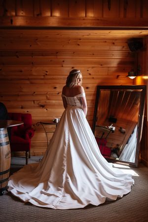A bride in a flowing white wedding dress sits on the floor in a rustic wood-paneled room, with varying light angles.