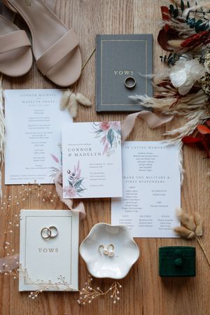 Elegant wedding stationery and invitation suite with floral designs laid out on wooden surface with rings and decorative elements.