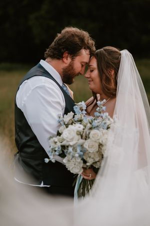 An intimate wedding moment captured as a couple shares a tender embrace while holding a delicate white and blue bouquet.