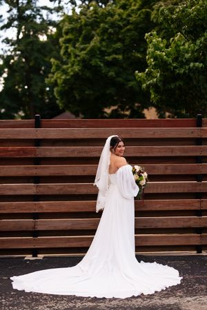 Bride in flowing white gown with long train poses against rustic wooden steps in garden setting.