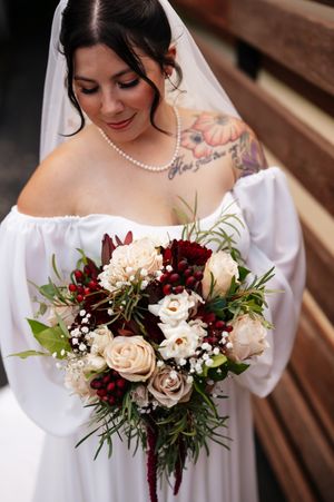 A wedding bouquet featuring burgundy and cream roses with delicate greenery against a rustic wooden background.