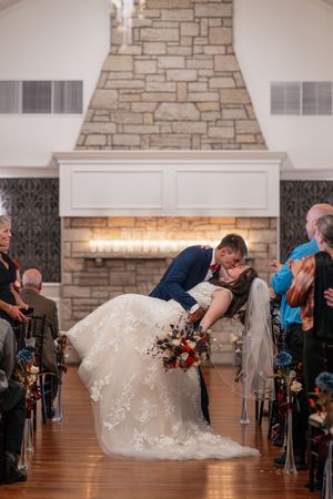 A romantic wedding ceremony moment showing a dramatic dip kiss in front of a stone fireplace.