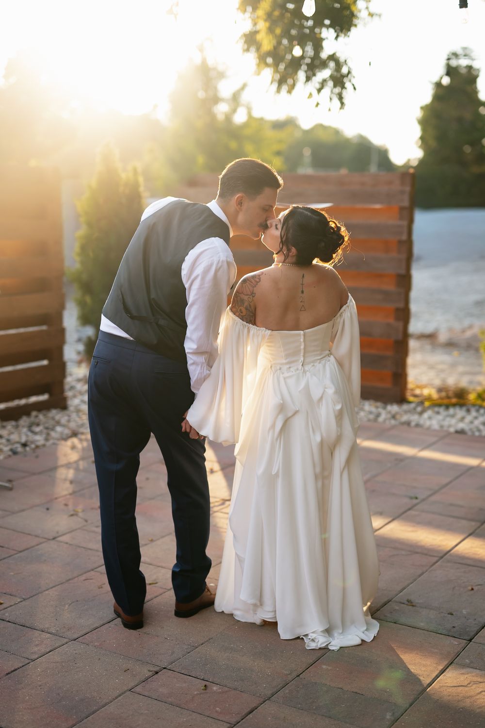 Newlywed couple sharing an intimate moment at sunset on a stone patio with wooden fence backdrop.