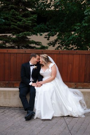 A romantic wedding photo series showing a couple sitting together on stone steps in front of a wooden fence.