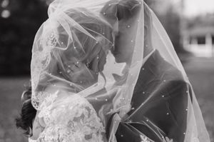 Black and white photo of a bride and groom sharing an intimate kiss under a flowing veil during their wedding ceremony.