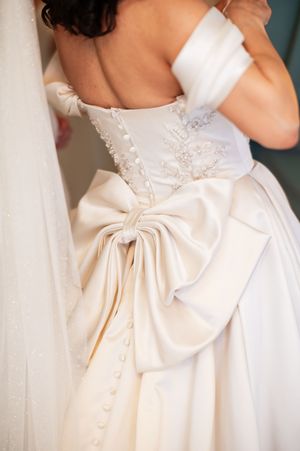 Back view of a bride in a white strapless wedding gown with lace bodice, large satin bow, and pearl buttons.