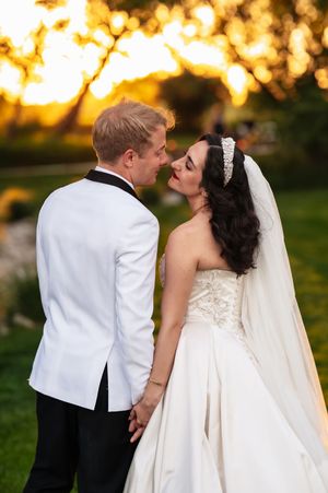 A bride and groom share a romantic moment at sunset, with the groom in a white tuxedo and bride in a strapless gown.
