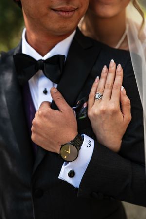 Bride and groom at wedding, showing diamond ring and black watch with bow tie tuxedo.